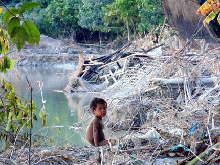 <p>A child sits amid remains of a collapsed house near Brahmaputra river after flood waters entered Rekhachapori Village in Silapothar, Assam on Thursday (Image by Press Trust of India)</p>