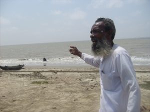 <p>Badruddin Sarkar stands atop a five-metre-high embankment and points to the tree stump, where his home used to be before it was drowned by the Bay of Bengal [Image by Joydeep Gupta]</p>