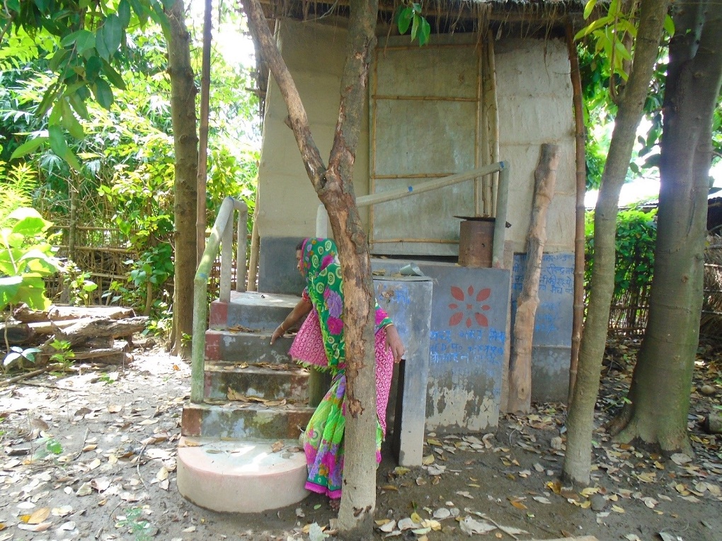 <p>A woman indicates the last flood water levels that inundated the Kairi village. The toilet was still accessible [image by: Aparna Unni]</p>