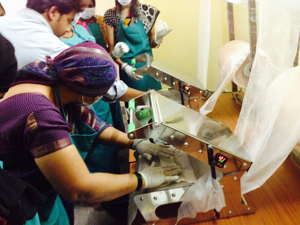 Women working on a manual sealing machine to manufacture the Anandi pad [image courtesy: Aakar Social]