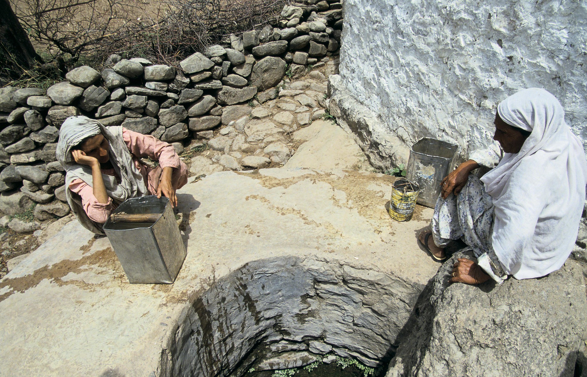 two people sitting near a well collecting water