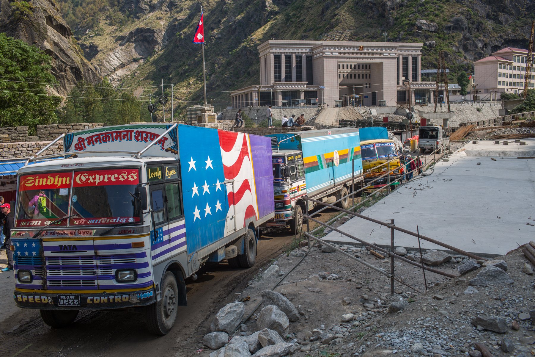 <p>Trucks entering Nepal from China at  Rasuwa Gadhi port. The Chinese Customs and Immigration office is in the background. Image source: Nabin Baral</p>