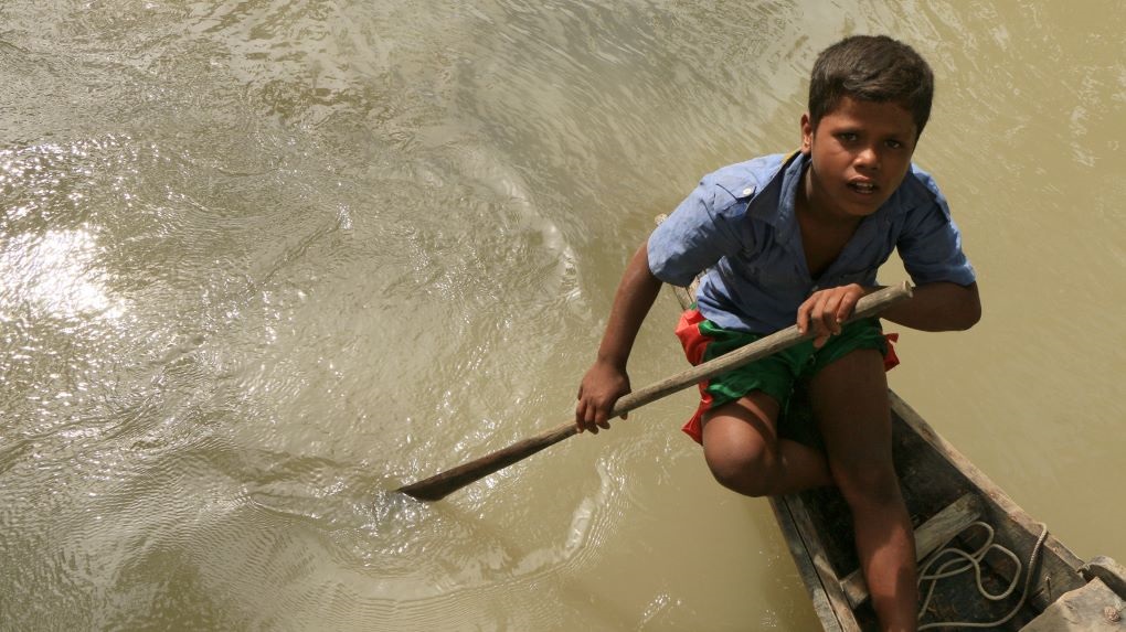 child on a boat wading through water in Bangladesh
