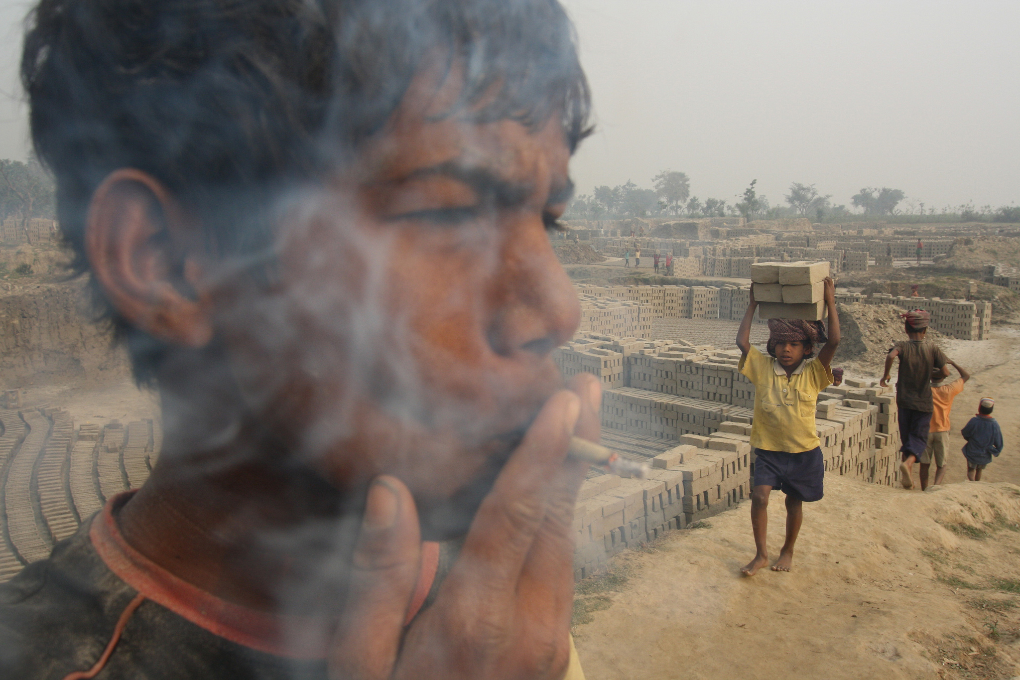 Clild labour in South Asia, sucheta Das. child smokes whilst boy carries building materials behind him