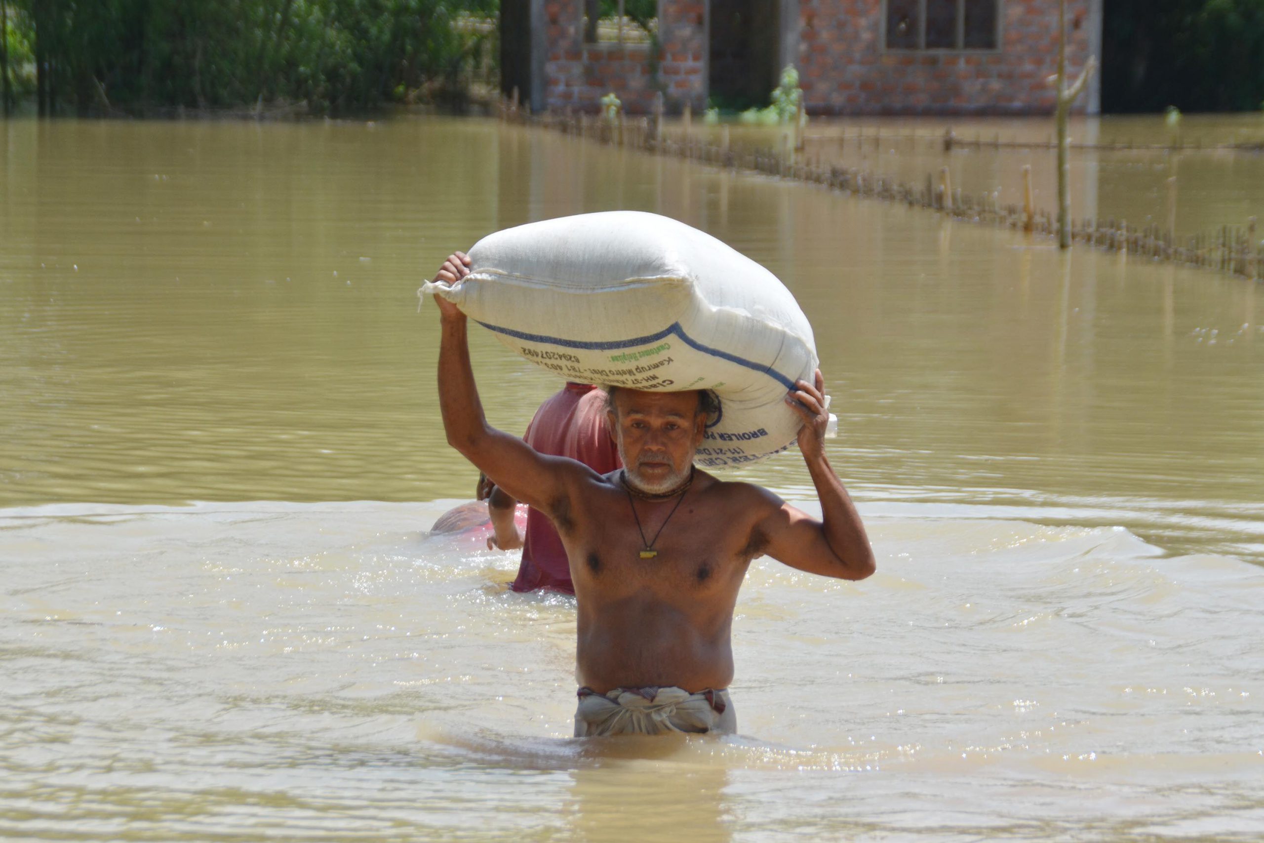 <p>A resident of Tetelisara village in Assam’s Nagaon district carries out his foodgrain stock as his home is flooded [image by: Diganta Talukdar/Alamy]</p>