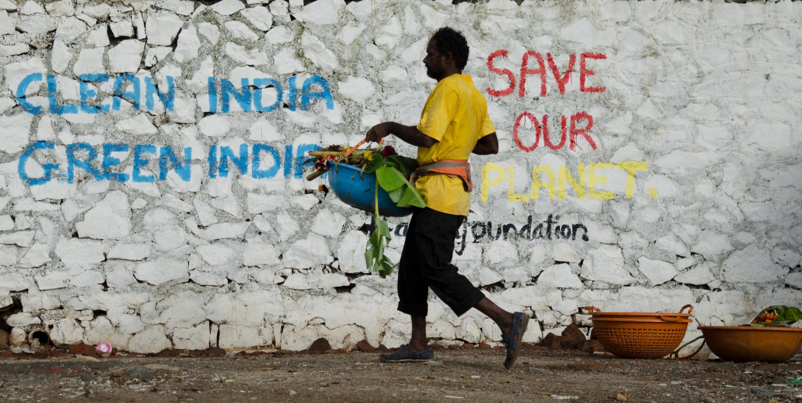 Man cleaning beach in India. Wall with background text 'Clean India, Green India' and 'Save our Planet'
