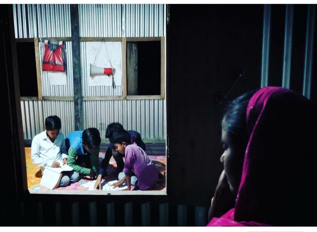 A woman looks on as children study at the library in the char [image by: Rituparna Neog]