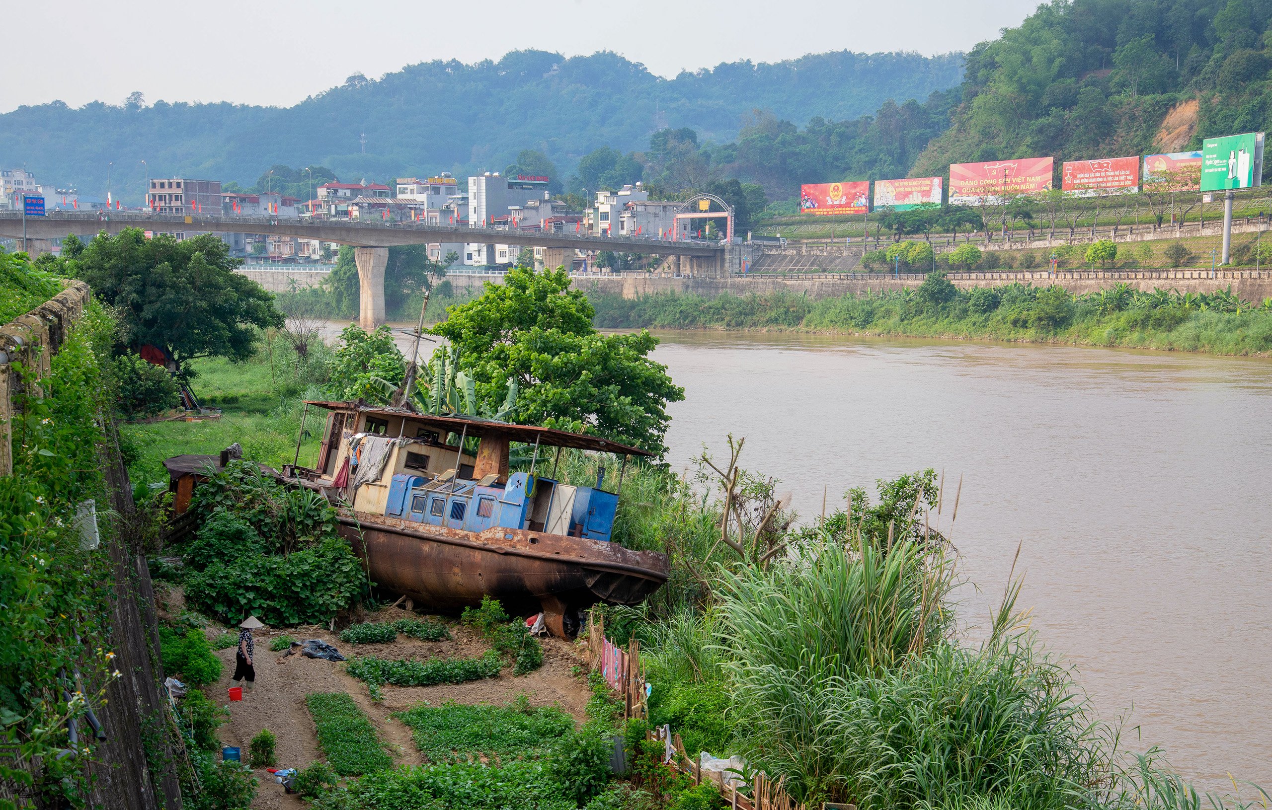 <p>The Red River in the city of Lao Cai in Vietnam, just south of the border with China. This boat had been trapped under the Coc Leu bridge (pictured in the background) for two years before being washed free by a flood in 2020 (Image: Linh Pham)</p>