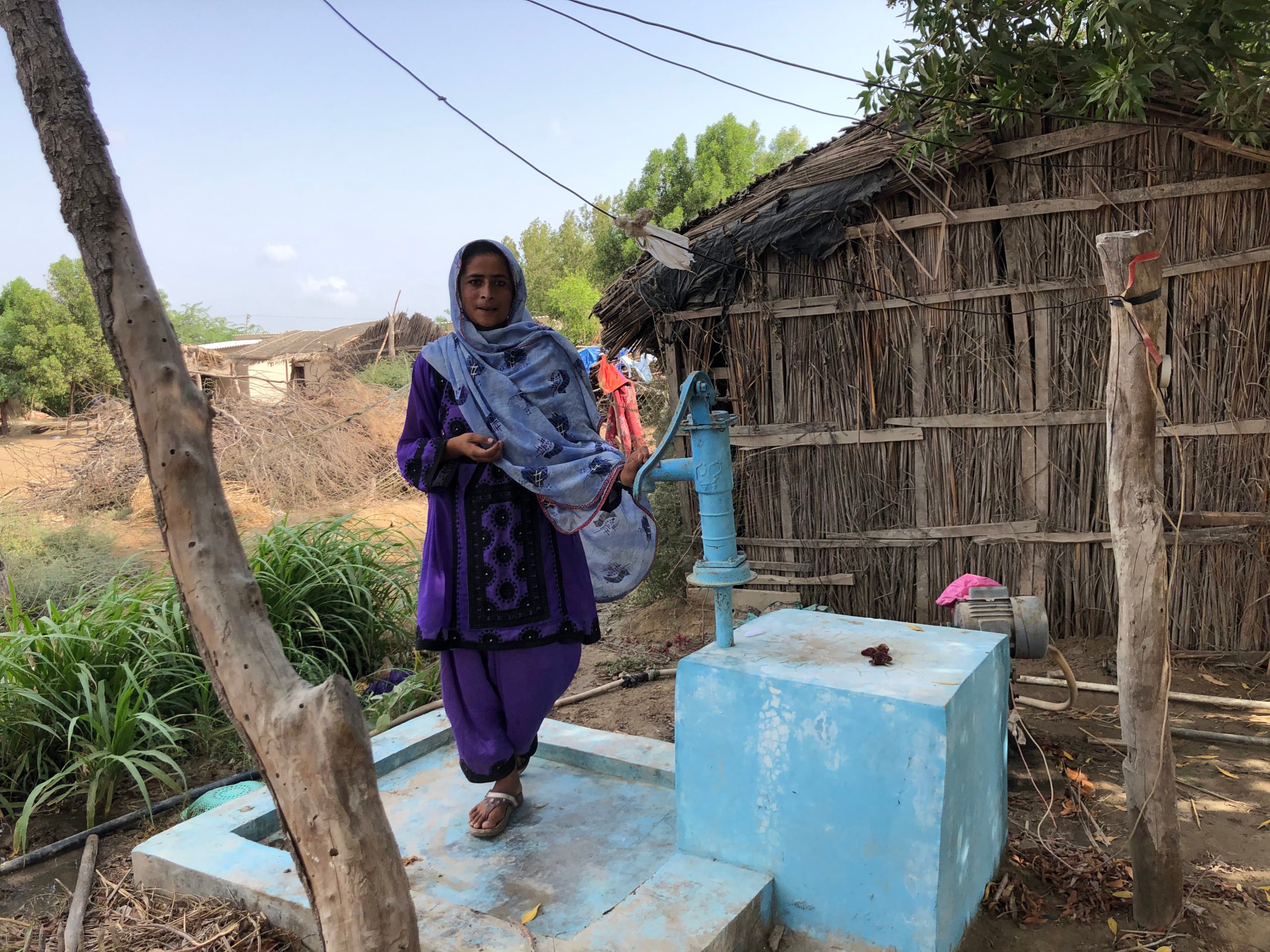 <p>Malda Barkat stands next to a hand pump near her house in the village of Rato Khan Rind, in Thatta district. The intermittent supply means villagers must fetch water from a distance on a donkey cart (Image: Zofeen Ebrahim)</p>