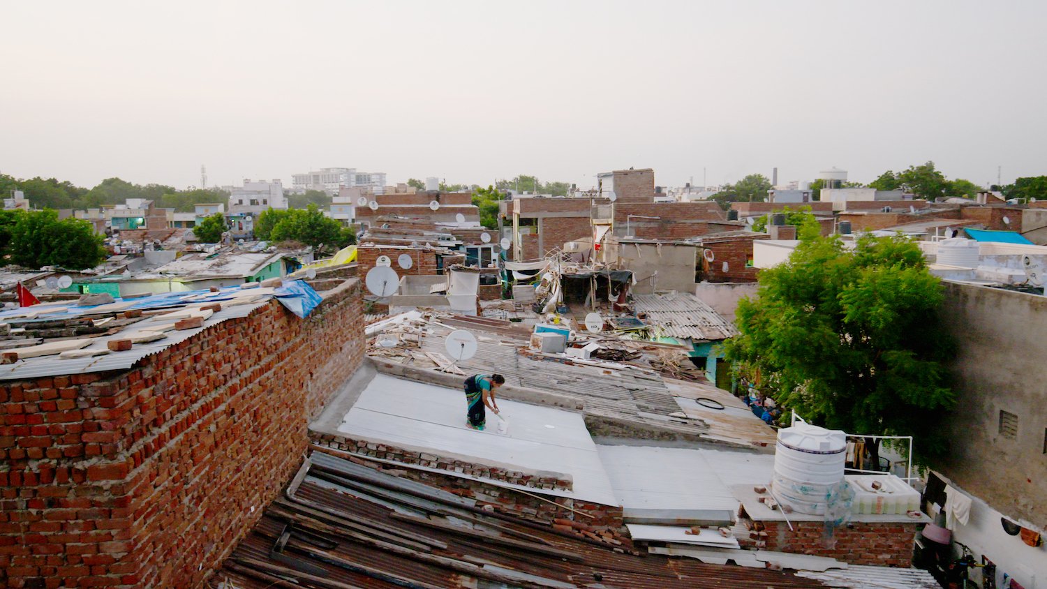 <p>Umaben Metkal paints the roof of her home in Saraspur, Ahmedabad, with solar-reflective white paint. Mahila Housing Trust has helped more than 2,500 households paint their roofs, which can reduce indoor temperatures by 4-5C. (Image: Ashden)</p>