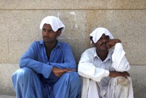 Men sit in the shade with water-soaked towels on their heads