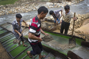 <p>Chinese gold miners shovel silt at a river mining site in 2014 in Kachin State, Myanmar. Gold mines like this use mercury in an environmentally hazardous extraction process, which can lead to long-lasting damage to forests and waterways. (Image: Taylor Weidman / Alamy)</p>