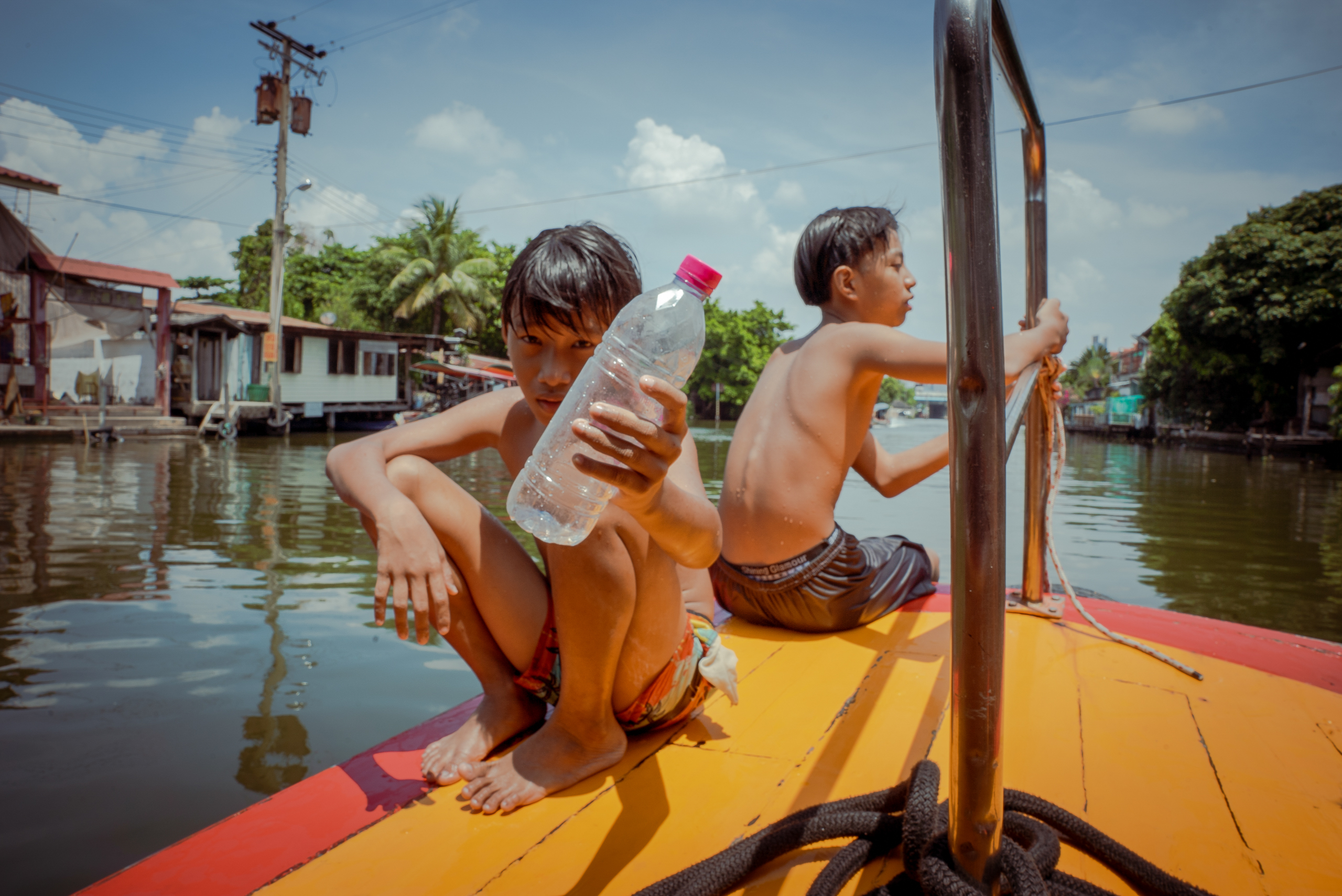 children on floating vessel, one holding empty plastic bottle