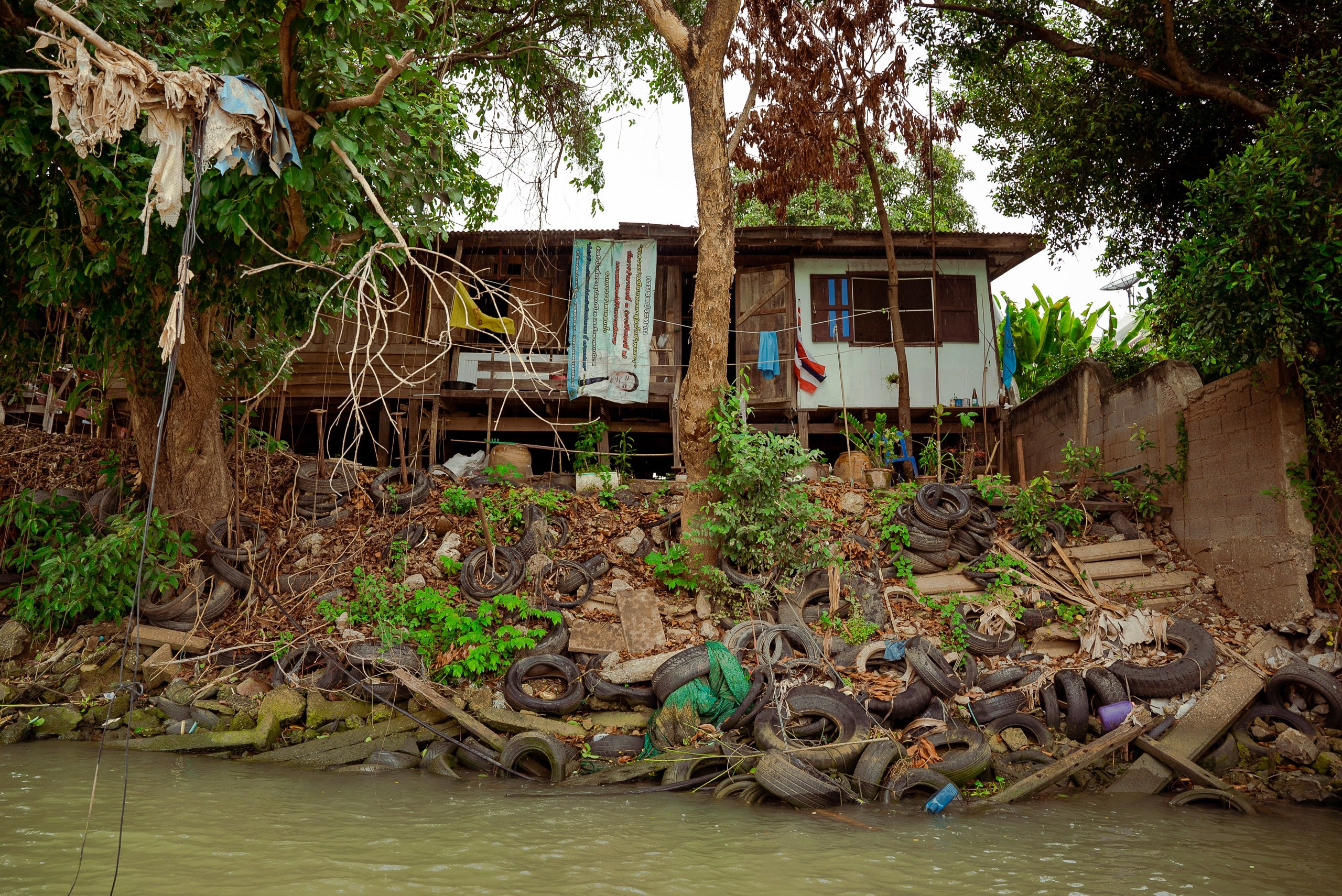 house on stilts near river with several old tyres at river's edge