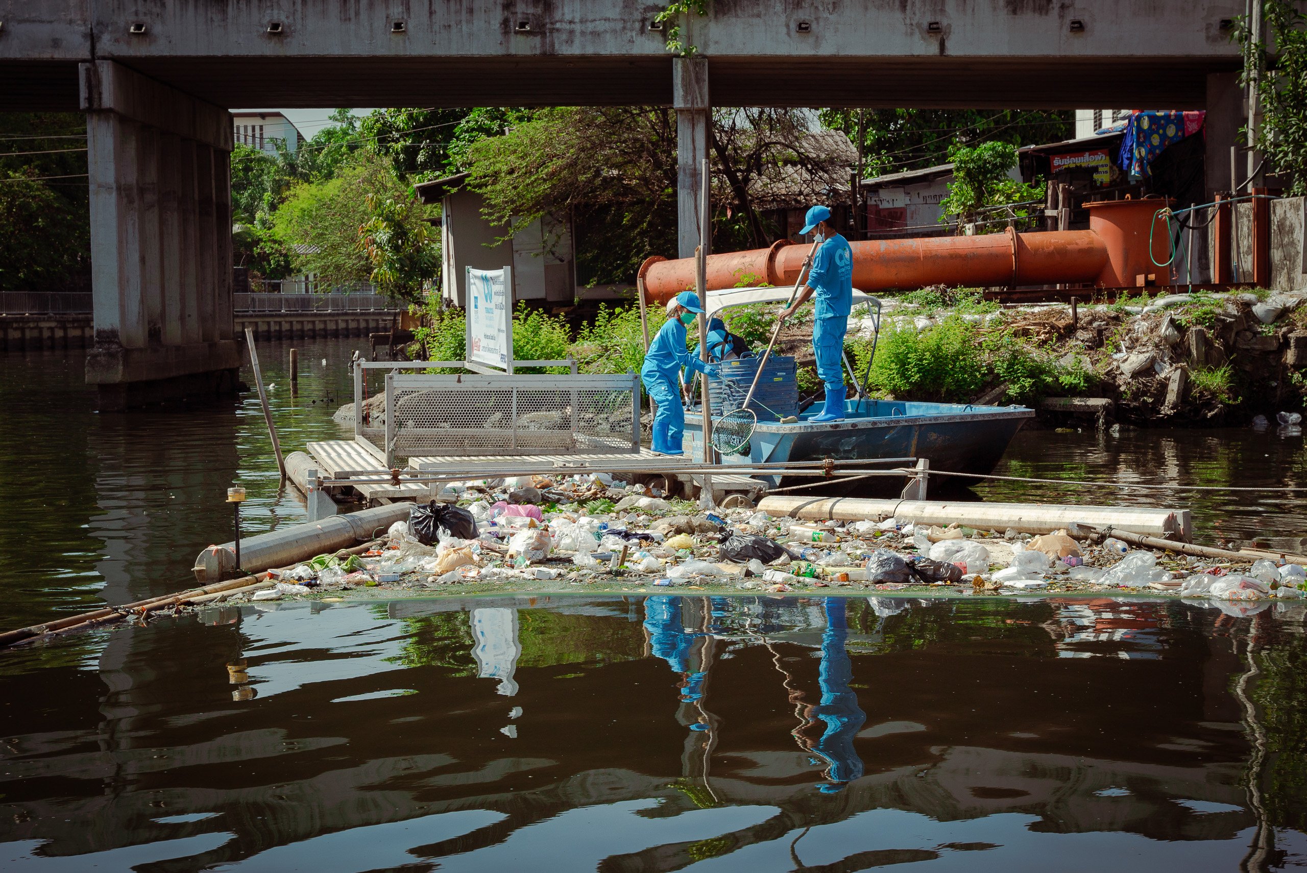 two people in blue uniforms reaching out towards floating river garbage with nets