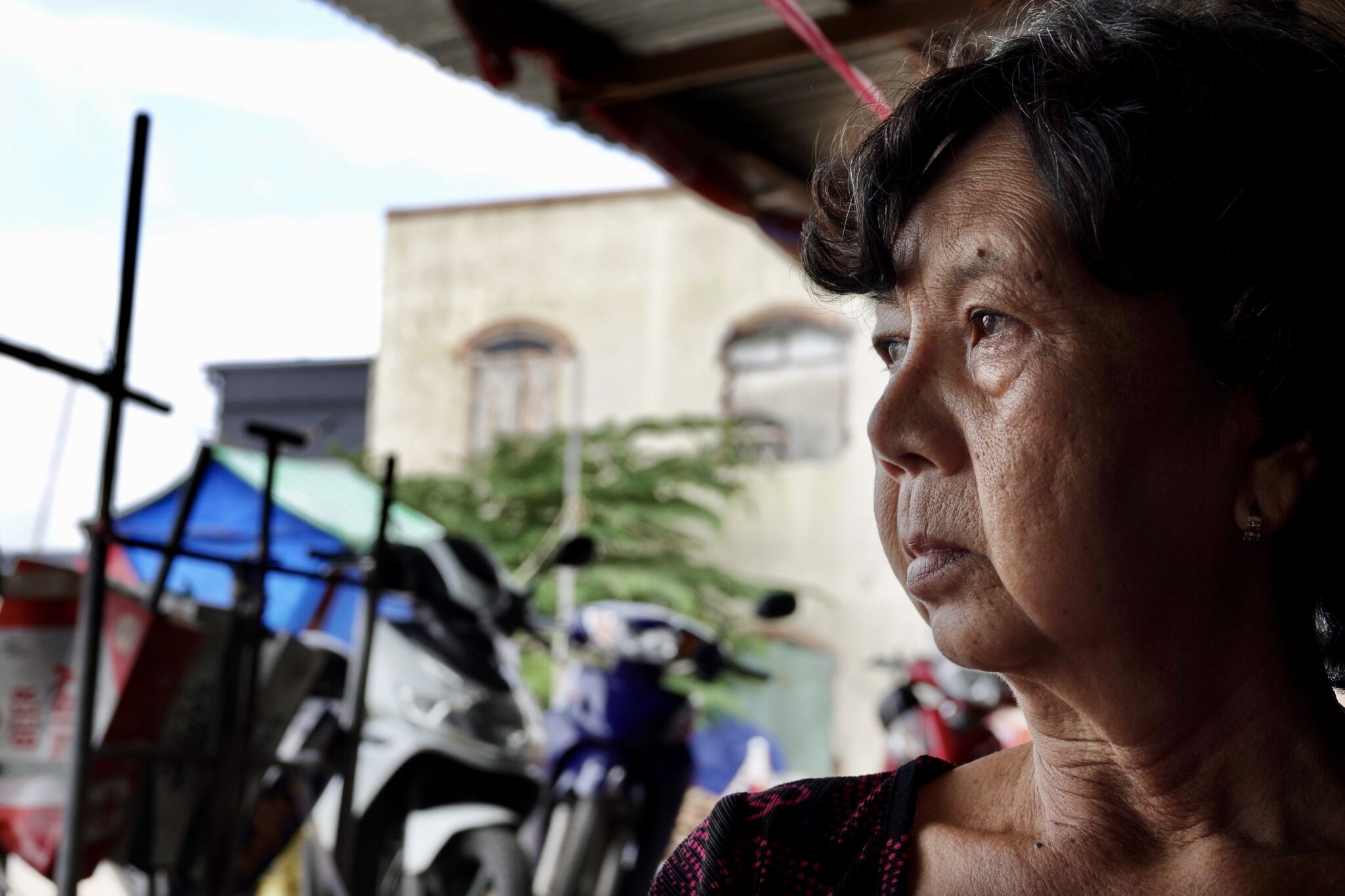 elderley woman looks into the distance in front of motorbikes: To Thi Kim Hong has decided to move back to her house despite the risks of subsidence because otherwise, she has no livelihood.