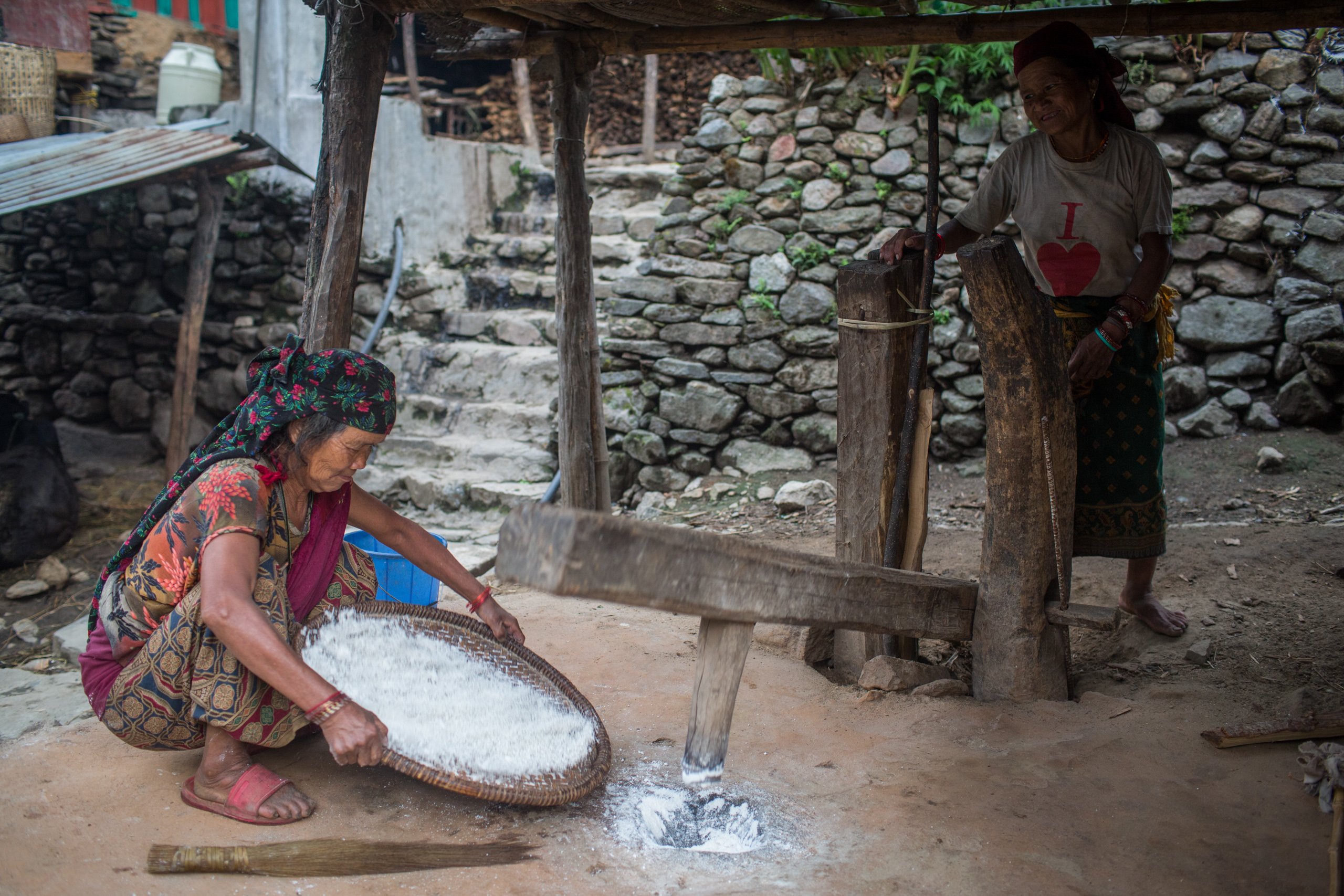Gurung women in Naiche grind rice in a dhiki, a traditional manual grinder. Women tend not to be involved in honey hunting as they are busy with household work.