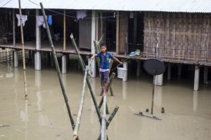 <p>A boy crosses a bamboo bridge to fetch drinking water during a flood in 2014 in Dikhowmukh, a Mising village in Assam (Image: Alamy)</p>