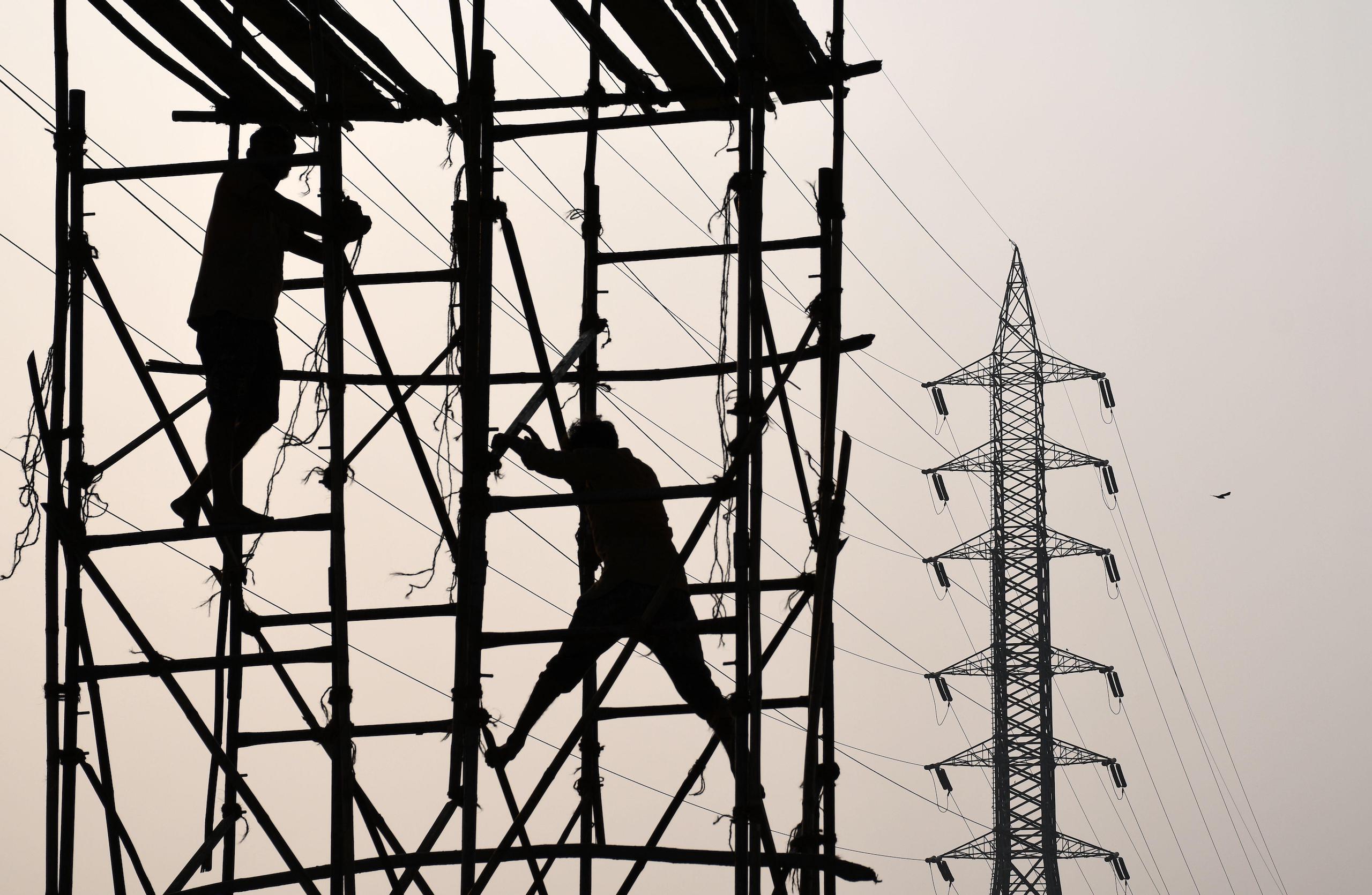 <p>Workers on bamboo scaffolding near electricity pylons in Mumbai. One of the obstacles to India reaching its pledged 50% installed electricity generation capacity from non-fossil fuel sources is the fact that there has been little progress in modernising the electricity transmission and distribution network so that it can handle decentralised power-generation sources. (Image: Alamy)</p>