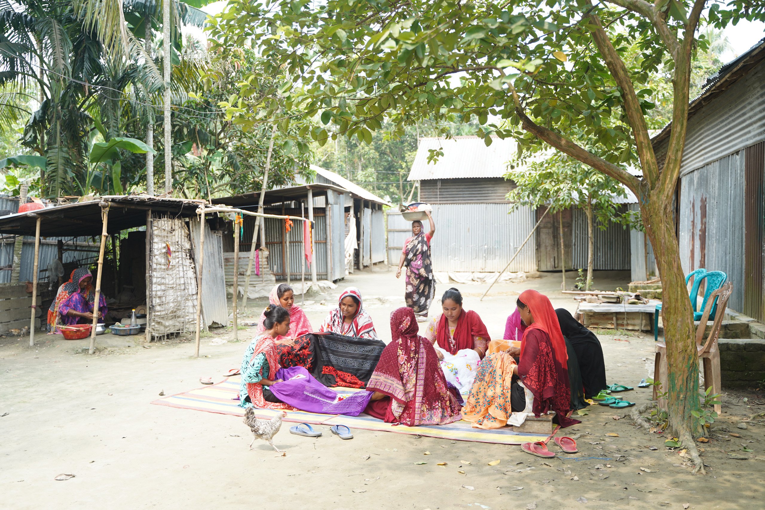 group of women sitting under tree with cloth, sewing