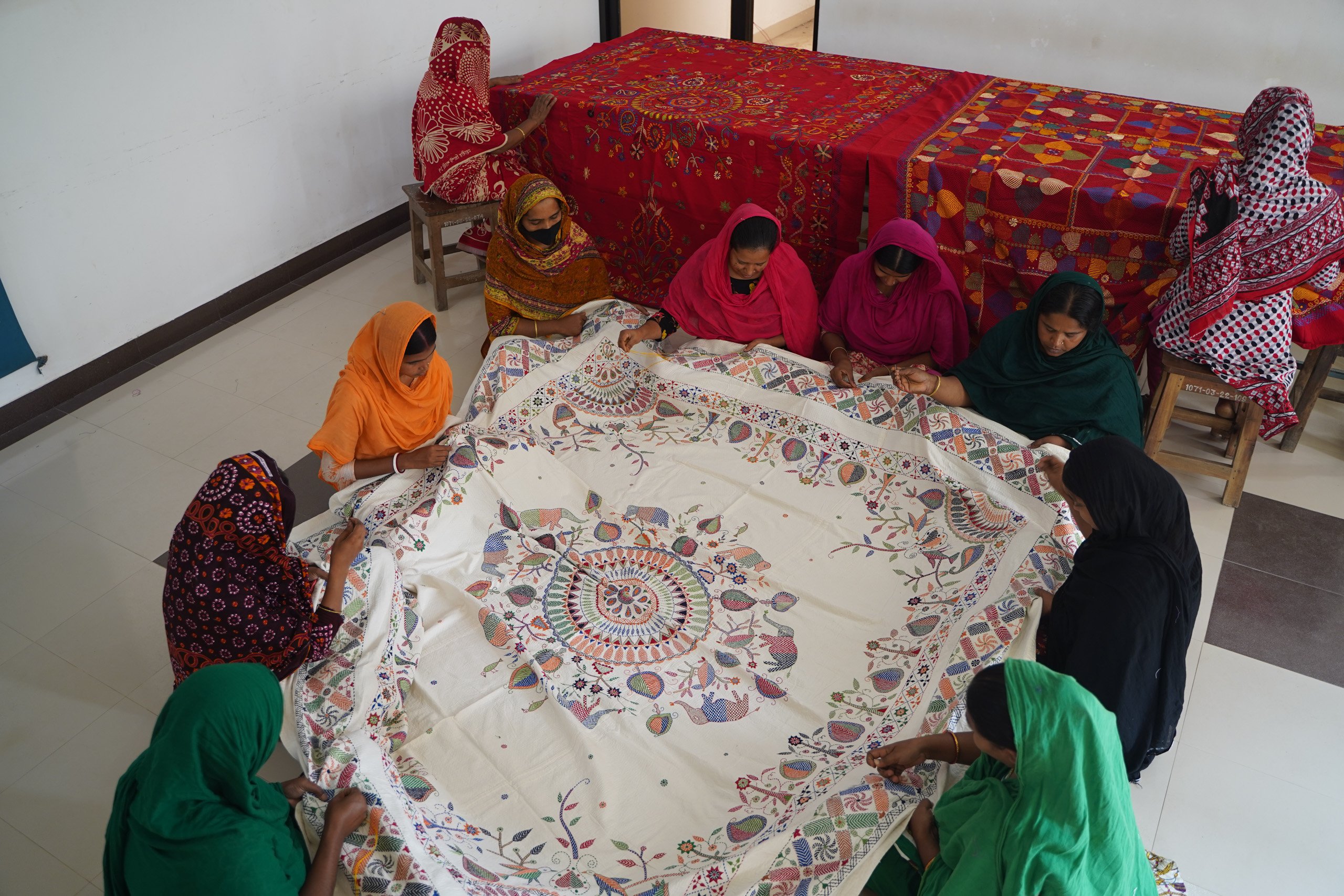 group of women embroidering borders of large white cloth