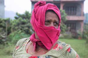 a woman in Nepal with bloodshot eyes wears a pink face covering to avoid dust pollution and looks away to the right