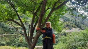 <p dir="ltr">चिपको आंदोलन के नेताओं में से एक की बहू, जूठी देवी, अक्टूबर 2022 में रैणी गांव में एक पेड़ के तने को पकड़े हुए दिख रही हैं। लगभग 50 साल पहले उत्तराखंड के रैणी में महिलाओं ने लकड़हारों से अपने जंगलों के पेड़ों को बचाने के लिए अपने शरीर आगे कर दिए थे। ऐसा करने से एक वैश्विक संरक्षण आंदोलन छिड़ गया था। (फोटो: वर्षा सिंह)</p>
