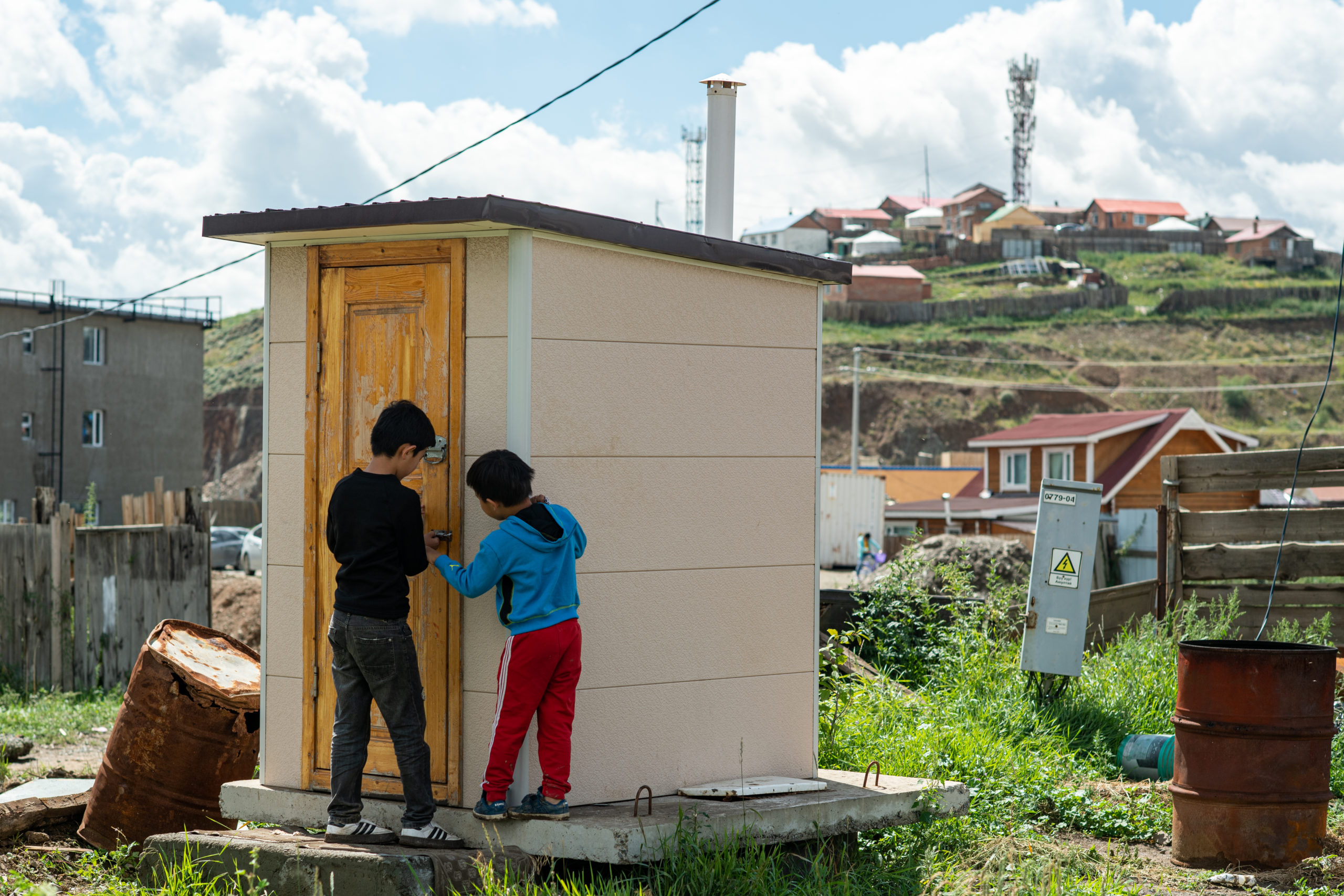 two children standing near outdoor toilet