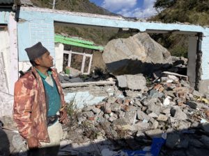 <p>Khamsung Tamang, a resident of Purano Syabrubesi village in Rasuwa district, central Nepal, stands in front of his neighbour’s destroyed house in December 2022. In August 2021, a landslide damaged 32 homes in the village; the villagers say it was caused by explosions for a hydropower project being built a few hundred metres away. (Image: Shristi Kafle)</p>