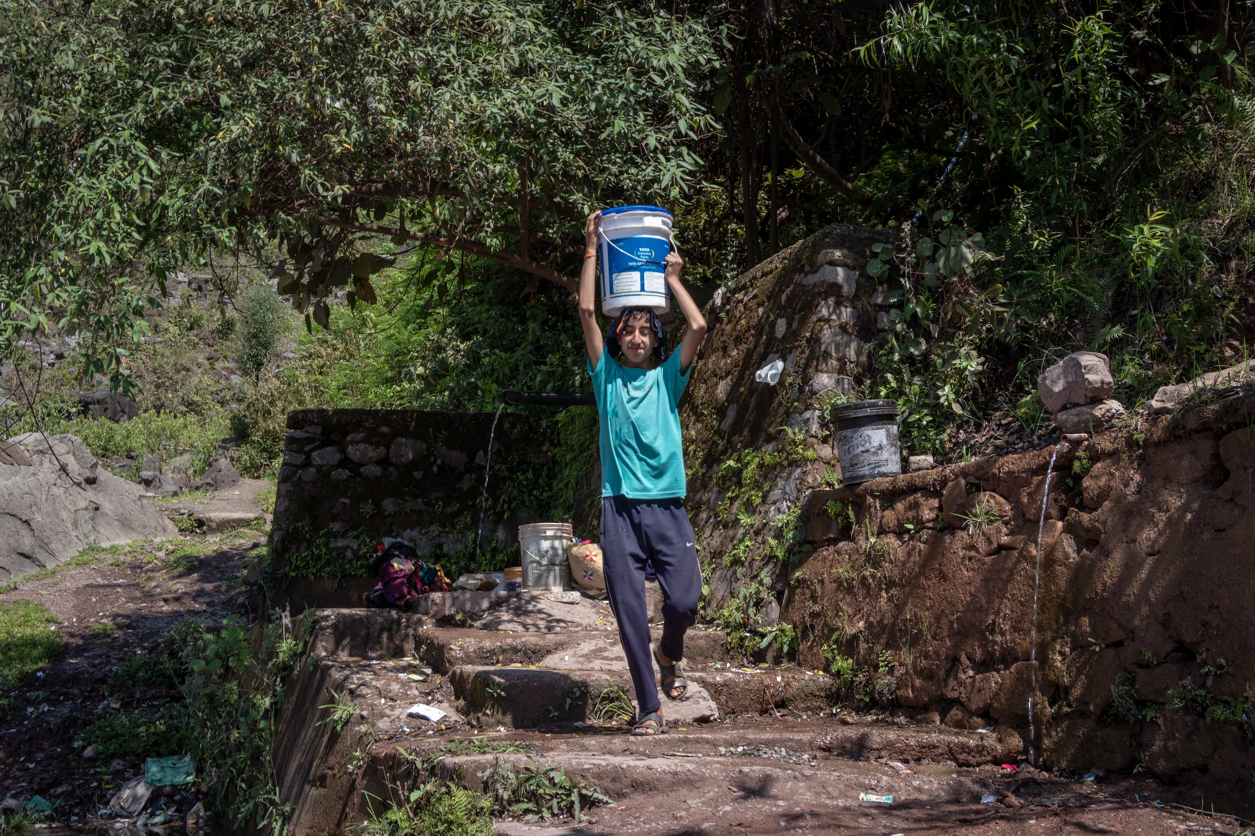 A boy carries a bucket of water after filling it from a nearby spring at Kauri village of Reasi