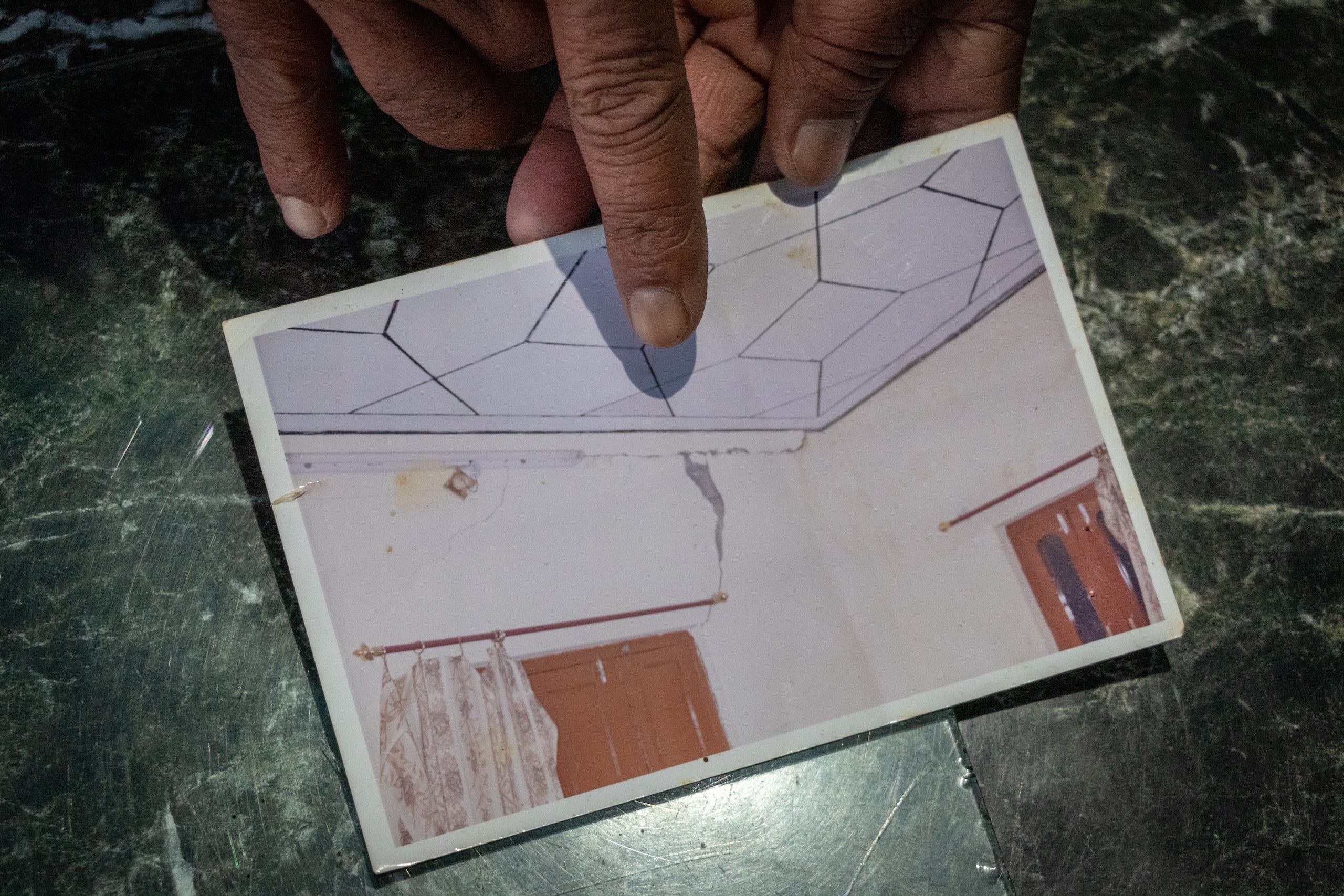 Nath shows a photograph while pointing to the cracks found on the walls of his house some 15 years back due to the construction of a dam in the nearby area of Salal. (Image: Ashish Kumar Kataria)