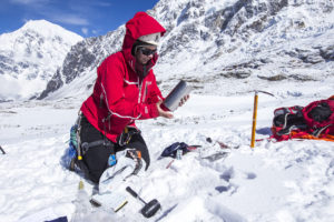 Scientist in red waterproof conducts research in snowy mountain landscape, Himalayas
