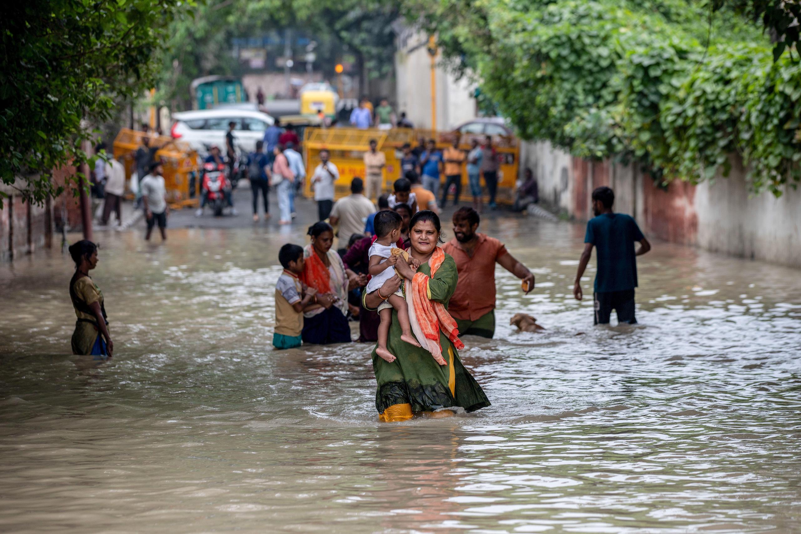 A woman holding a baby in her arm wades through a flooded road in New Delhi