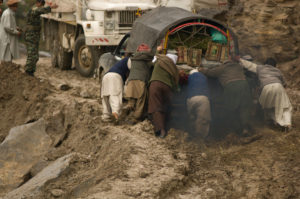 men try to push a truck that is stuck in mud and landslide debris