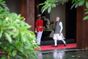 Indian prime minister Modi walks along a red carpet, green bushes in foreground