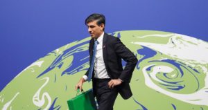 Rishi Sunak walks in front of a blue and green stylised image of the earth, holding a green briefcase