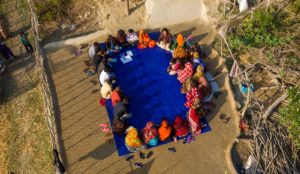 Aerial photo of people sat in a circle around a blue mat