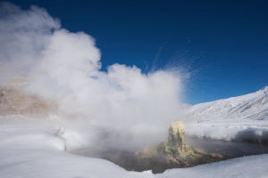 A geyser erupts in snowy mountain landscapes