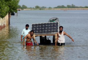 Three men wading through deep water carrying a solar panel
