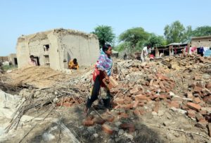 A woman carrying bricks across the remains of a collapsed house