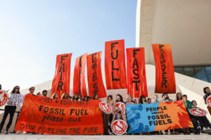 Group of young people hold red banners calling for a phase out of fossil fuels