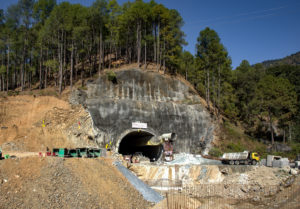 exit portal of large tunnel built into stony hill with construction equipment in foreground