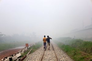 Two people walking in smog along train tracks